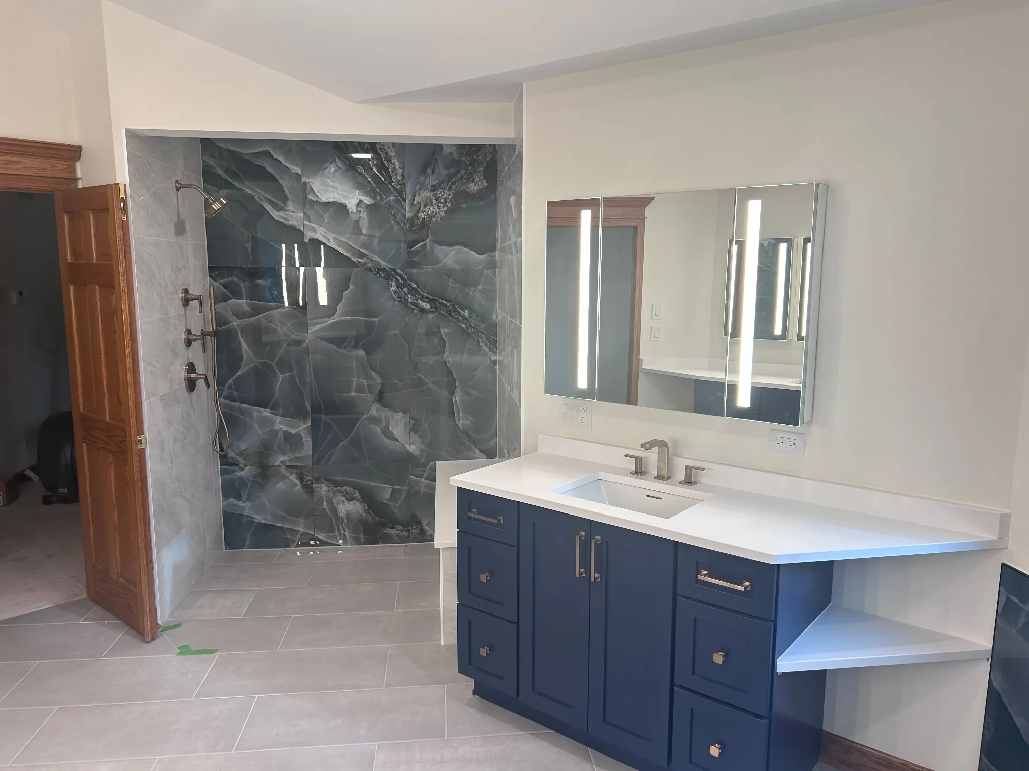 Kildeer bathroom remodel with a curbless shower, large-format tile, navy vanity, white countertop and LED medicine cabinet
