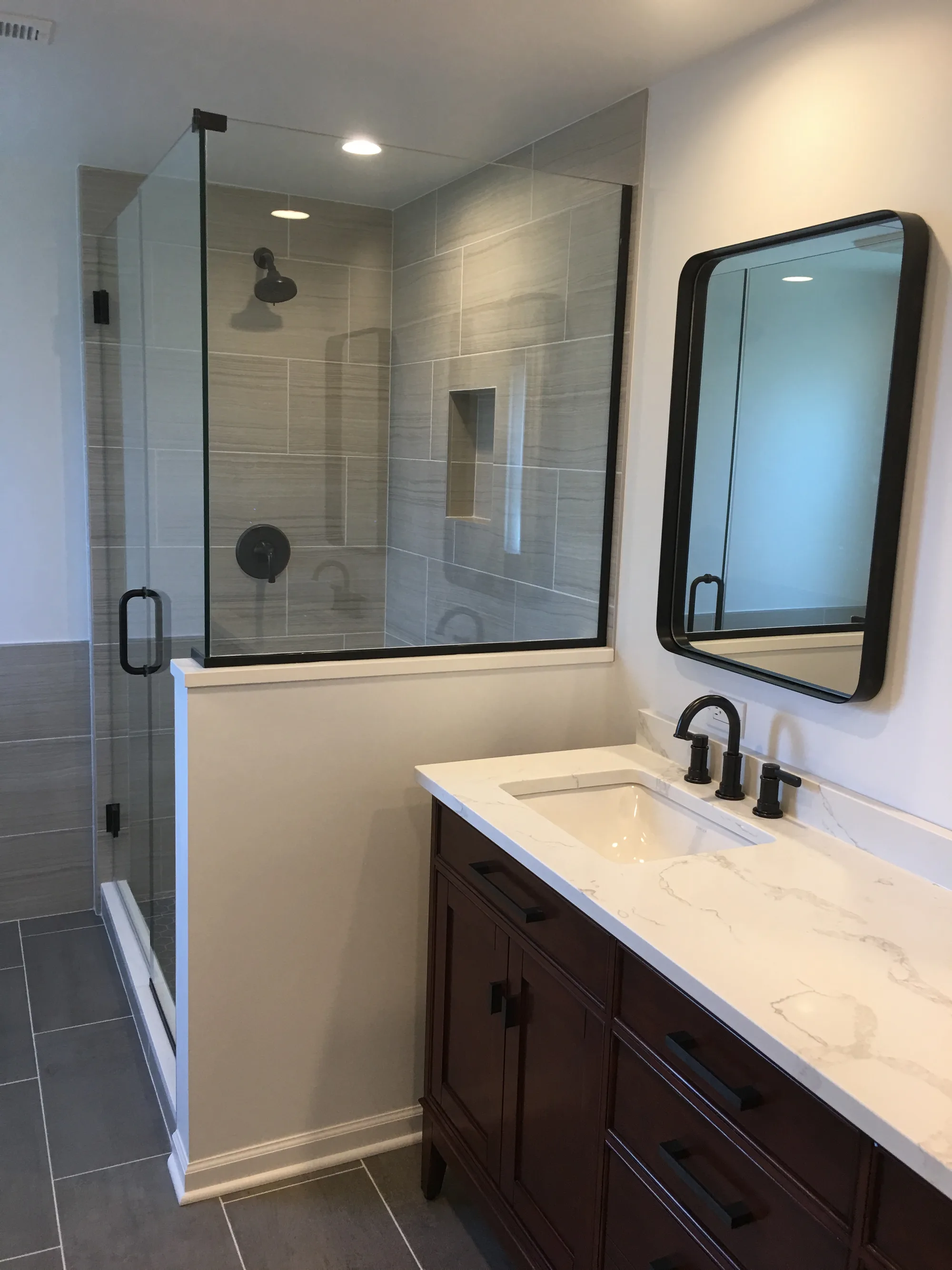Glenview bathroom by Delta: dark-stained wood vanity with calacatta quartz waterfall, frameless glass walk-in shower, oil-rubbed bronze faucet