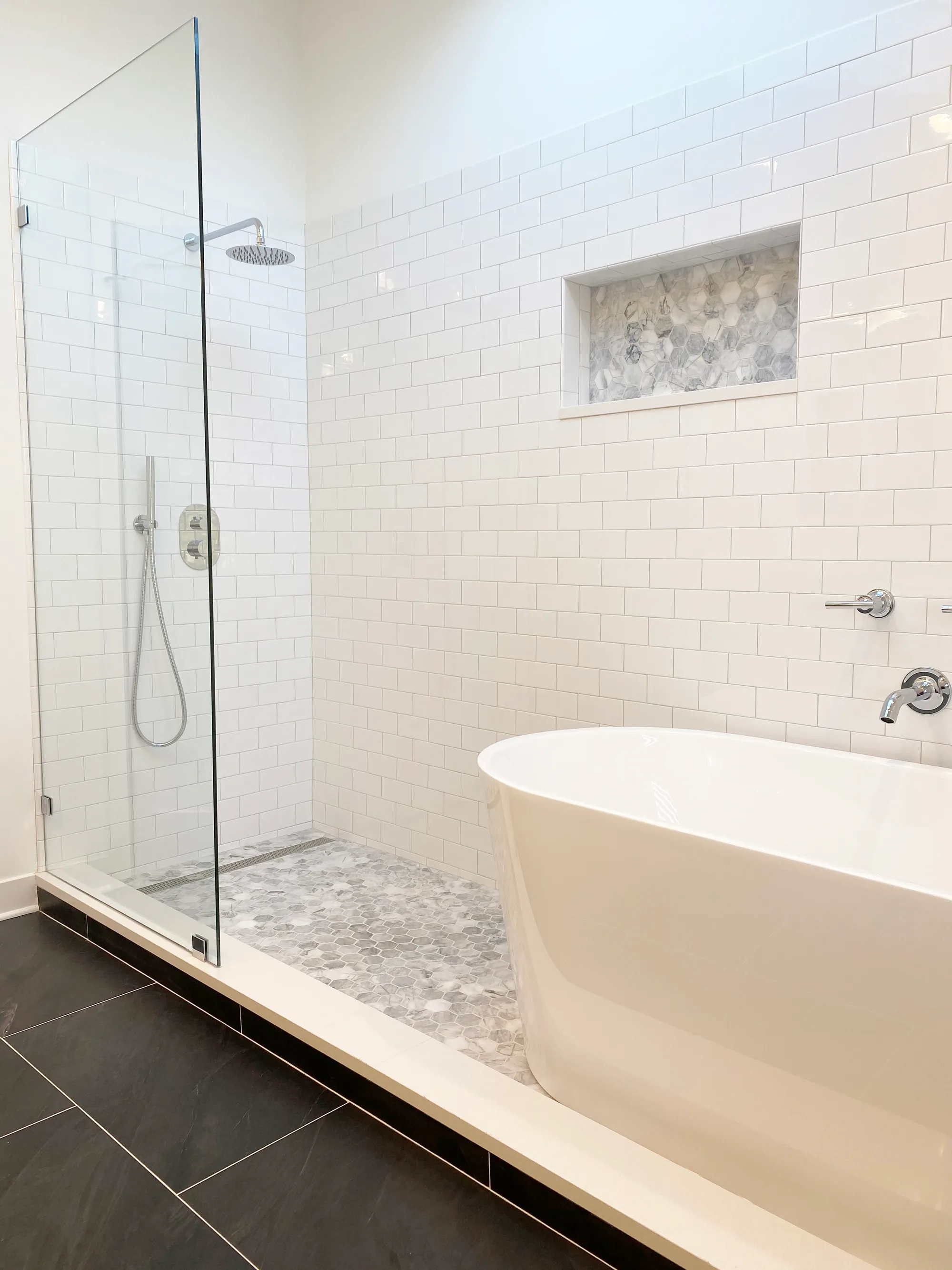 Highland Park bathroom by Delta: frameless glass walk-in shower with white subway tile, pebble mosaic floor, ceiling rainhead, freestanding tub