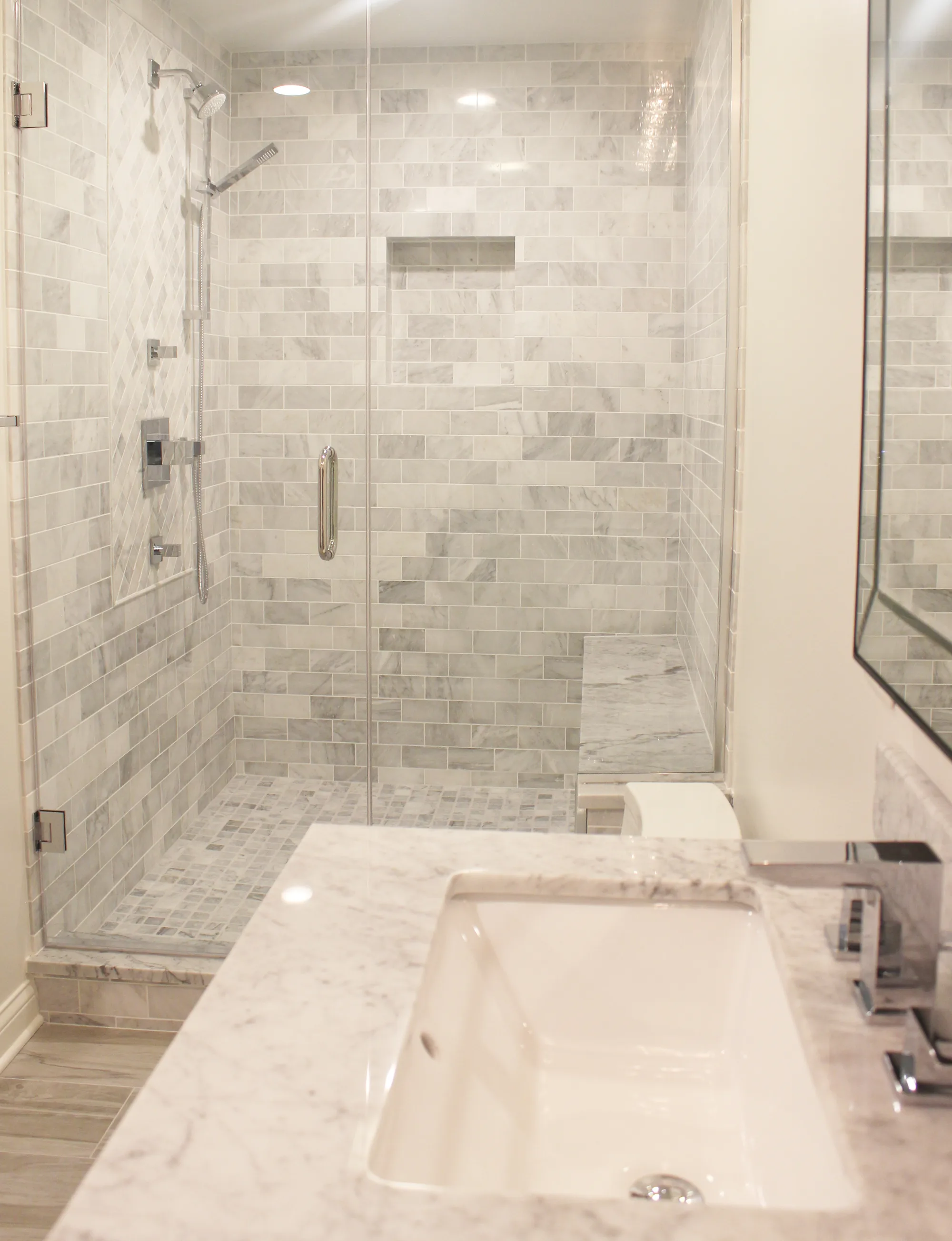 Highland Park primary bathroom by Delta: carrara marble subway tile walk-in shower, marble basket-weave floor, carrara marble counter, chrome faucet