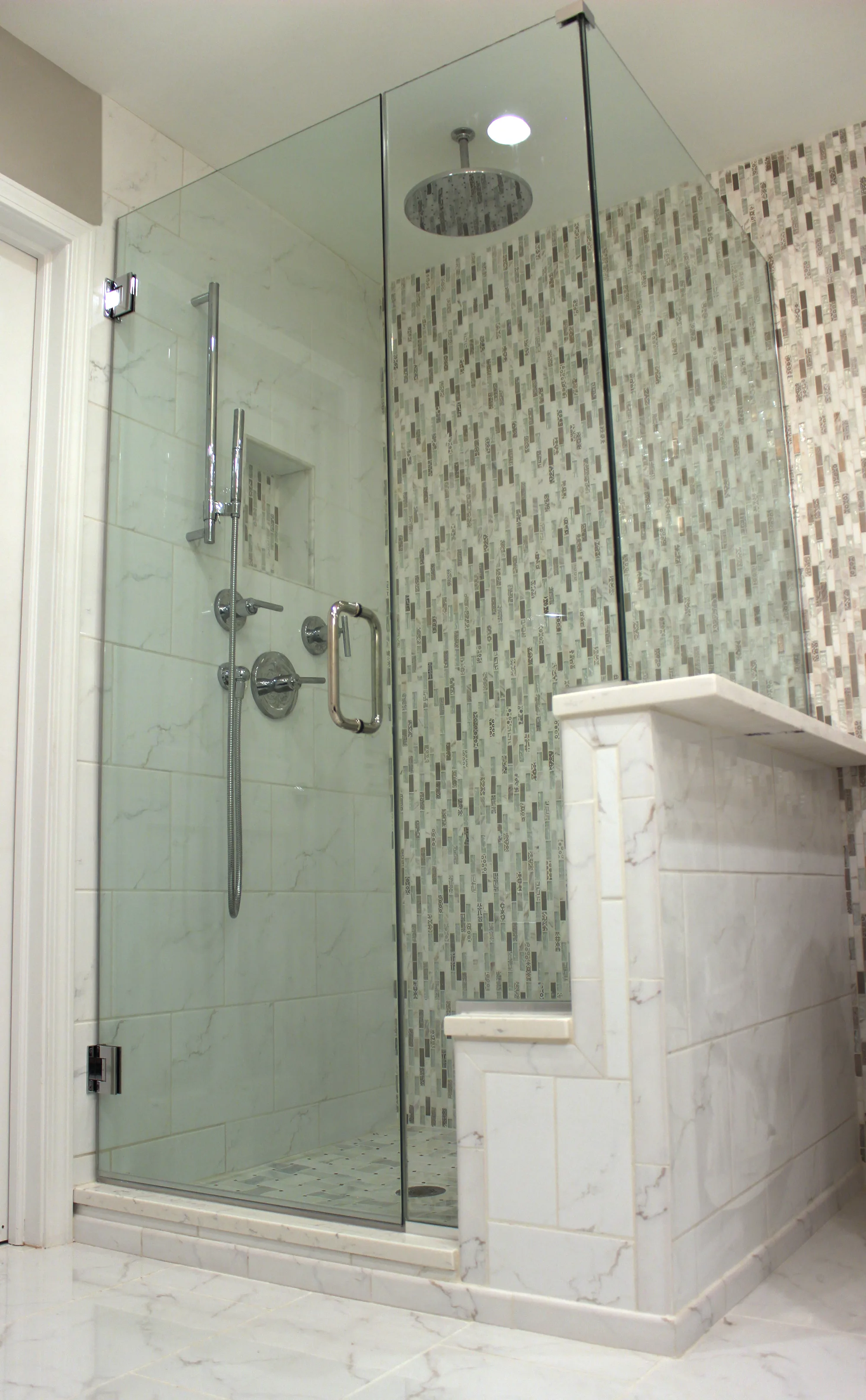 Highland Park bathroom by Delta: marble subway shower with vertical glass mosaic accent strip, ceiling rainhead, marble half-wall pony bench