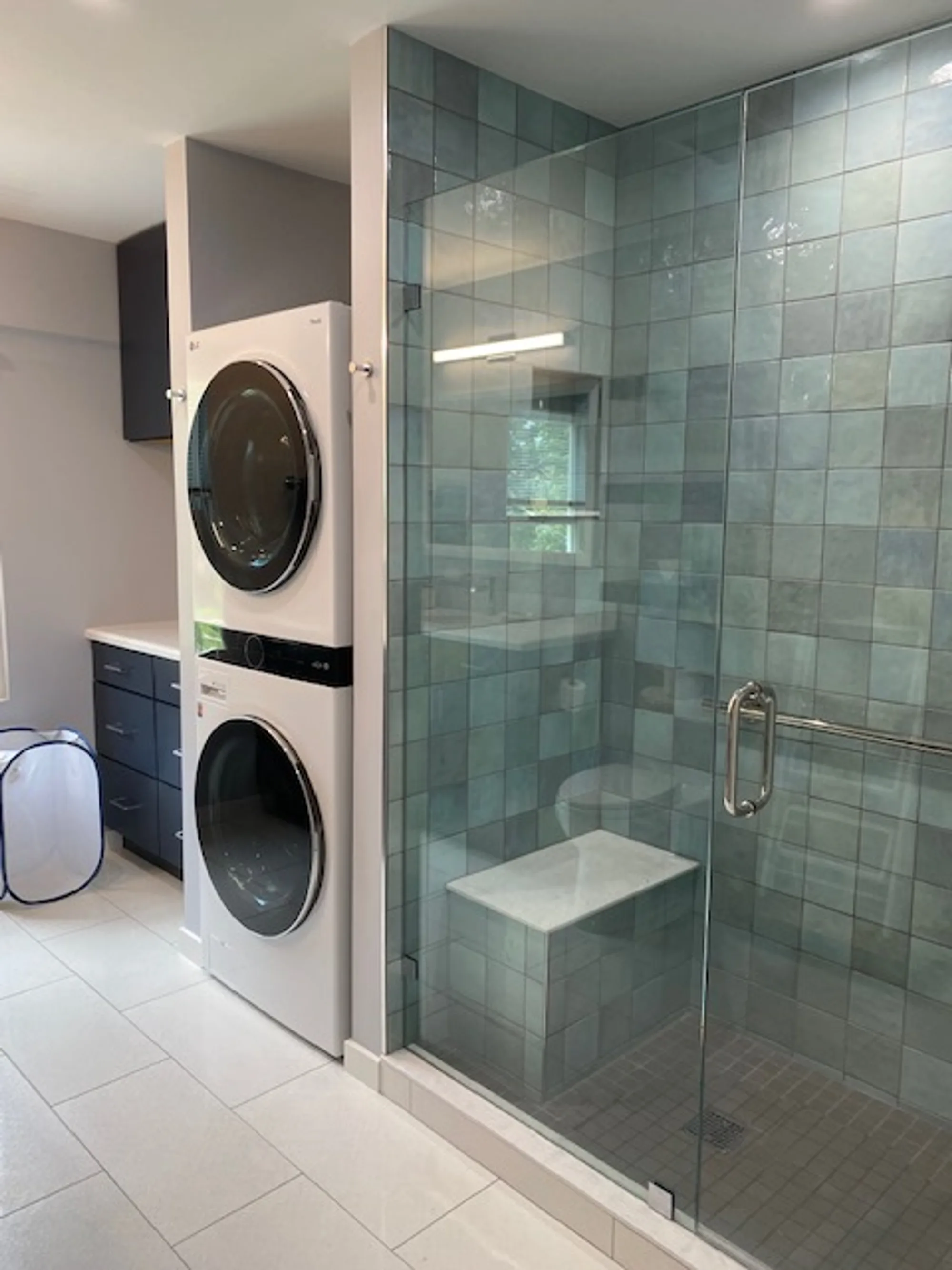 Highland Park bathroom by Delta: teal vertical glass-tile walk-in shower with marble bench, integrated stacked washer-dryer column, navy floating vanity