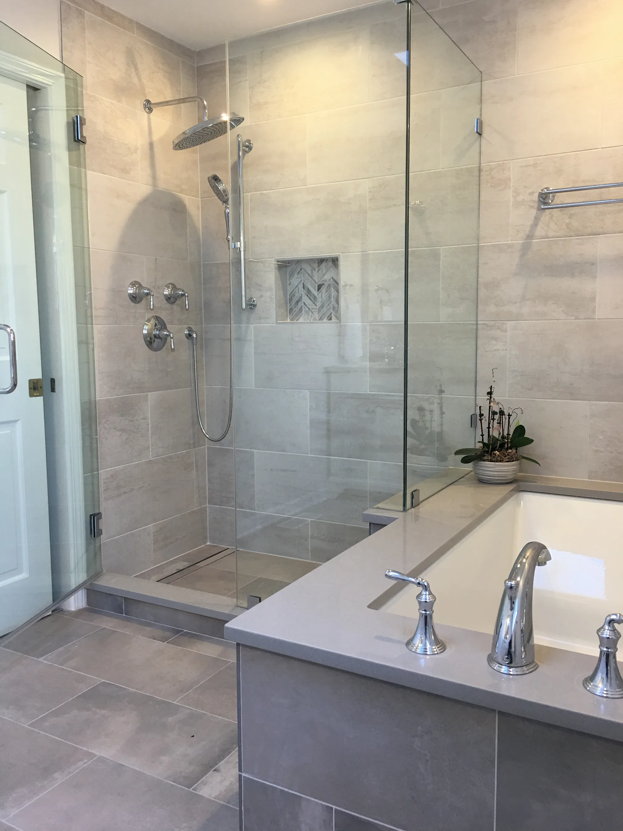 Lake Forest bathroom by Delta: frameless glass walk-in shower with large-format porcelain tile, herringbone marble niche, polished chrome rainhead, drop-in tub