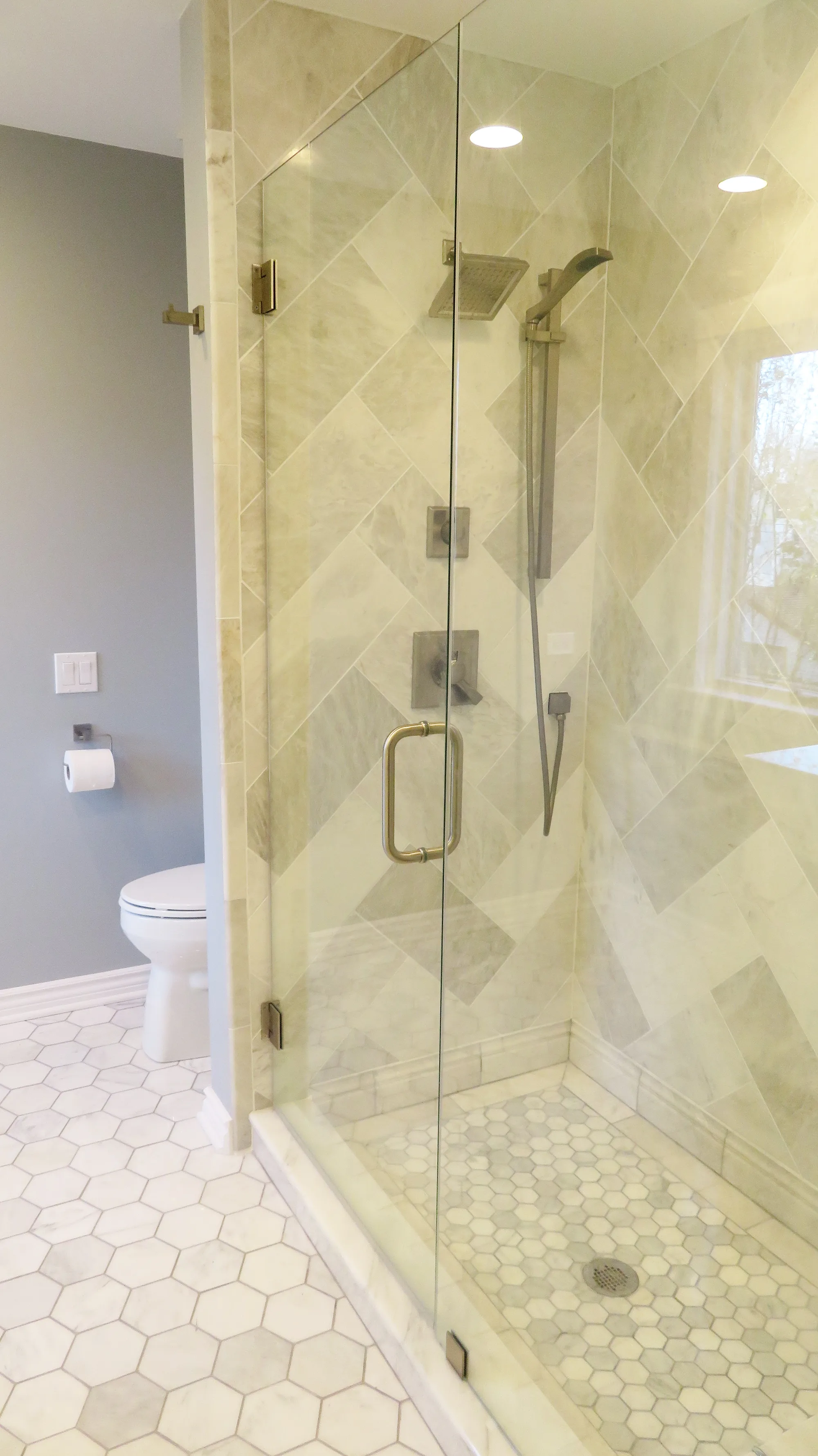 Wilmette bathroom by Delta: travertine diagonal-laid walk-in shower with hex marble mosaic floor, brushed nickel hardware, frameless glass