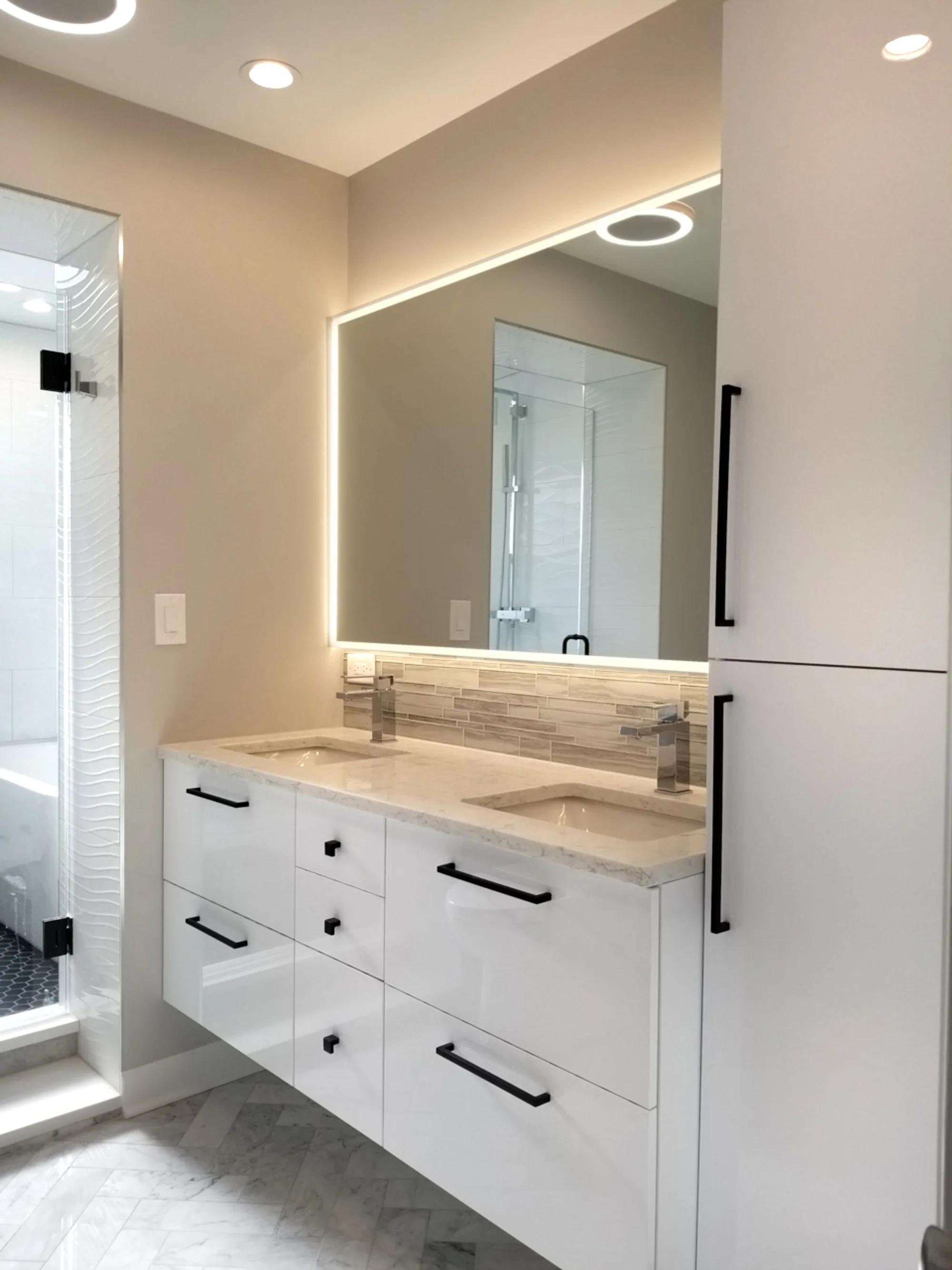 Winnetka bathroom by Delta: high-gloss white floating double vanity, backlit LED mirror, beige stone strip backsplash, matte black hardware