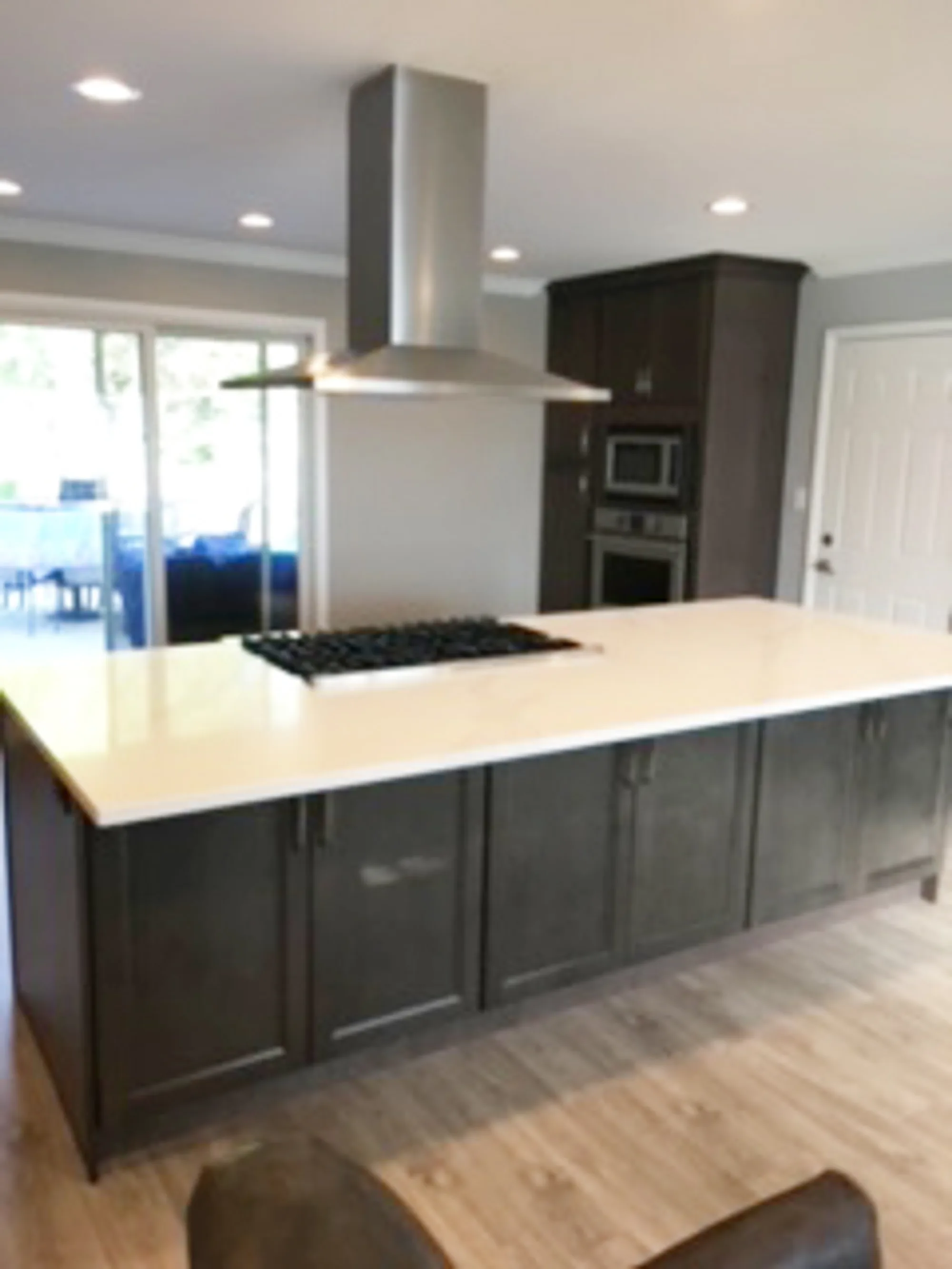 Glenview kitchen by Delta: oversized island with gas cooktop and stainless chimney hood, dark base cabinetry, double wall ovens