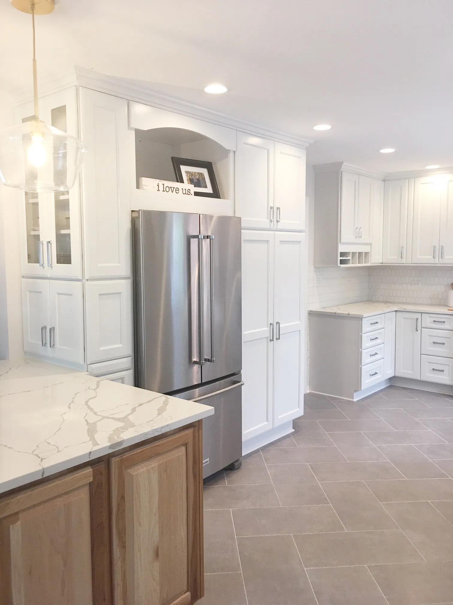 Lake Bluff kitchen by Delta: white shaker perimeter cabinetry, oak-base island with calacatta quartz waterfall, hexagonal mosaic backsplash, herringbone porcelain floor