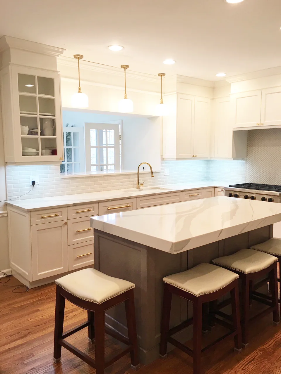Lake Forest kitchen remodel by Delta: white shaker cabinetry, calacatta marble waterfall island, three brass globe pendants, herringbone marble range wall