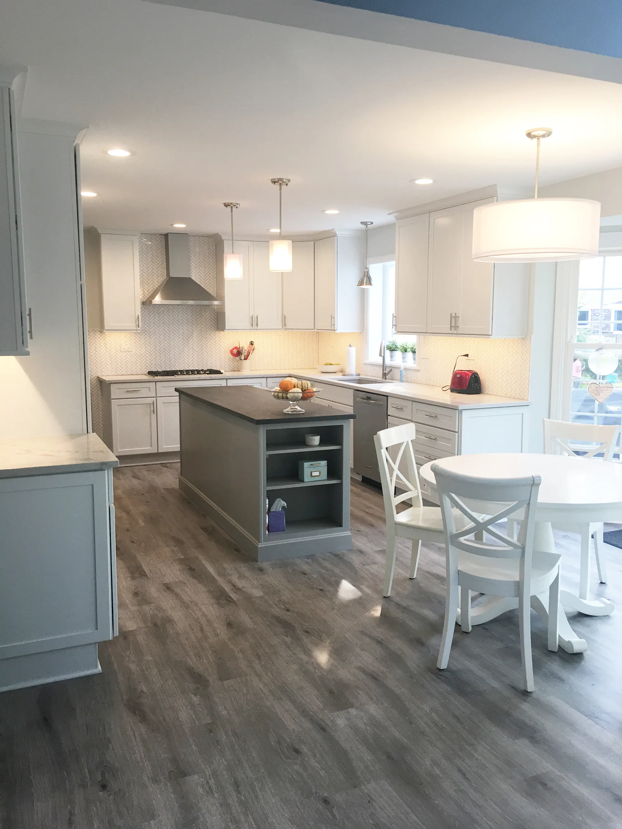 Northbrook kitchen by Delta: light gray shaker cabinetry, gray island with calacatta quartz, vertical herringbone backsplash, stainless chimney hood, drum pendants