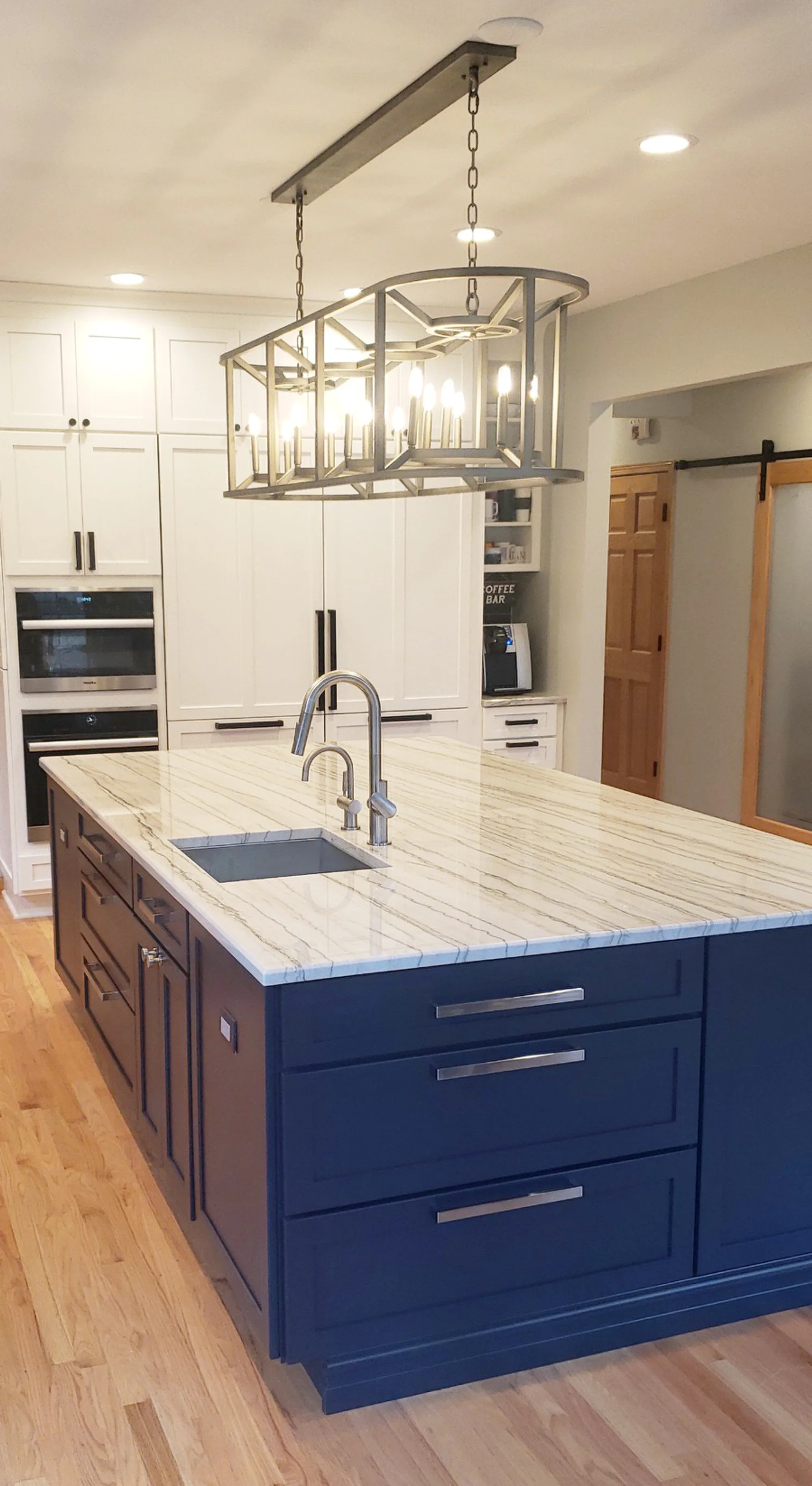 Wilmette kitchen by Delta: navy painted island with white marble waterfall, brass cage chandelier, double wall ovens, white shaker perimeter cabinetry