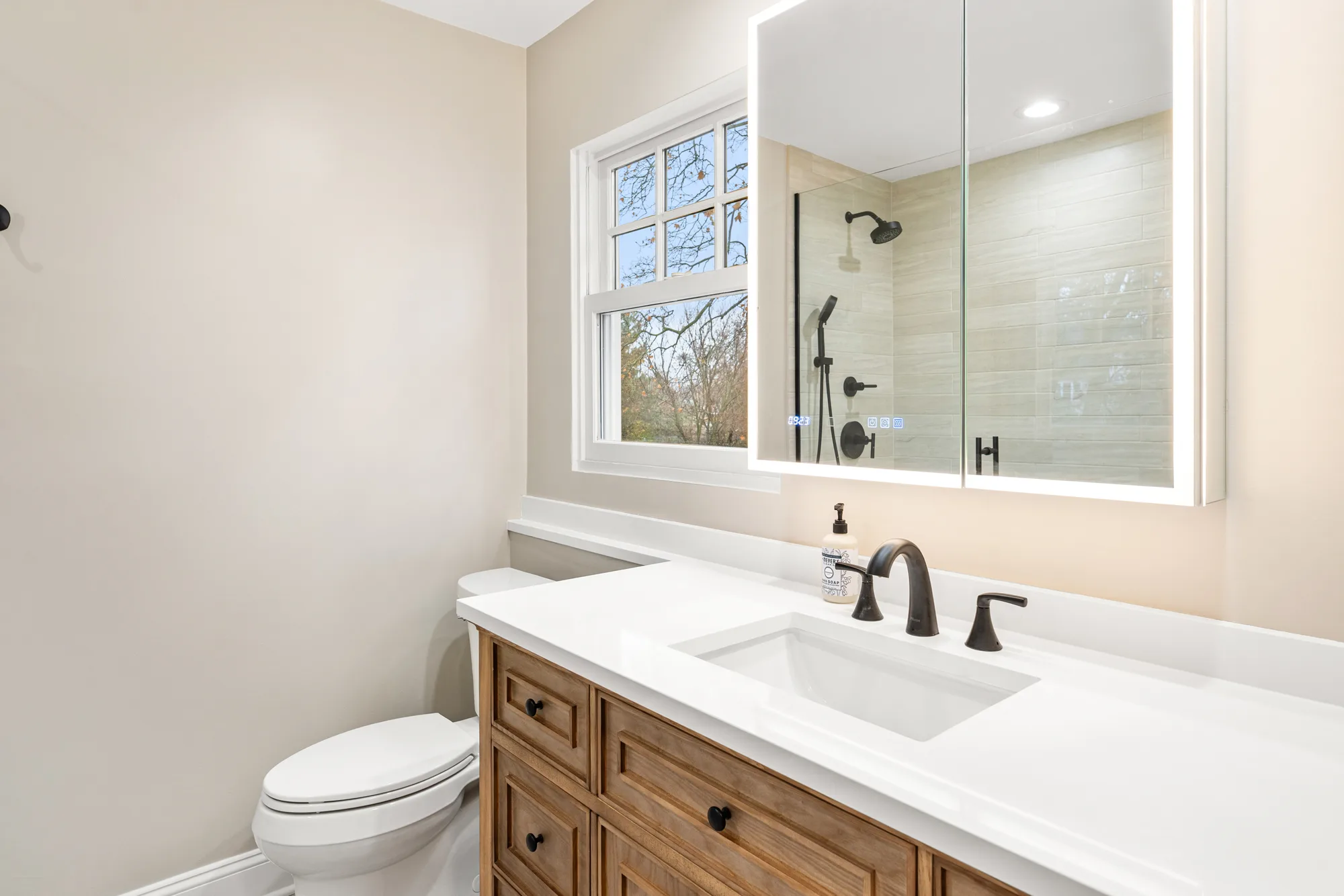 Stowe Court bathroom Northbrook by Delta: honey-oak vanity with white quartz counter, smart LED mirror with digital clock, matte black faucet