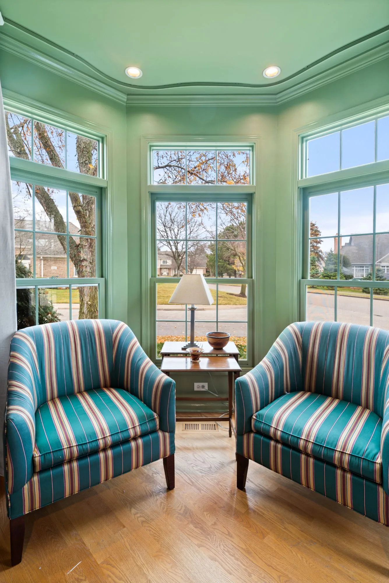 Bay window sitting area with two striped armchairs and green-painted window trim