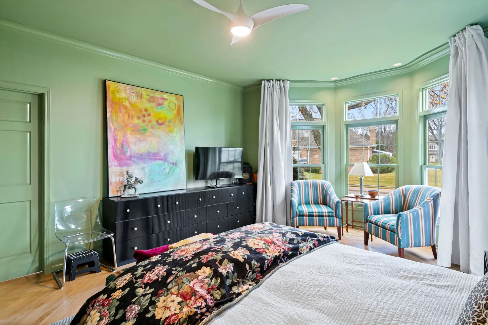 Primary bedroom dresser wall beside the bay windows, with oak floors and a ceiling fan