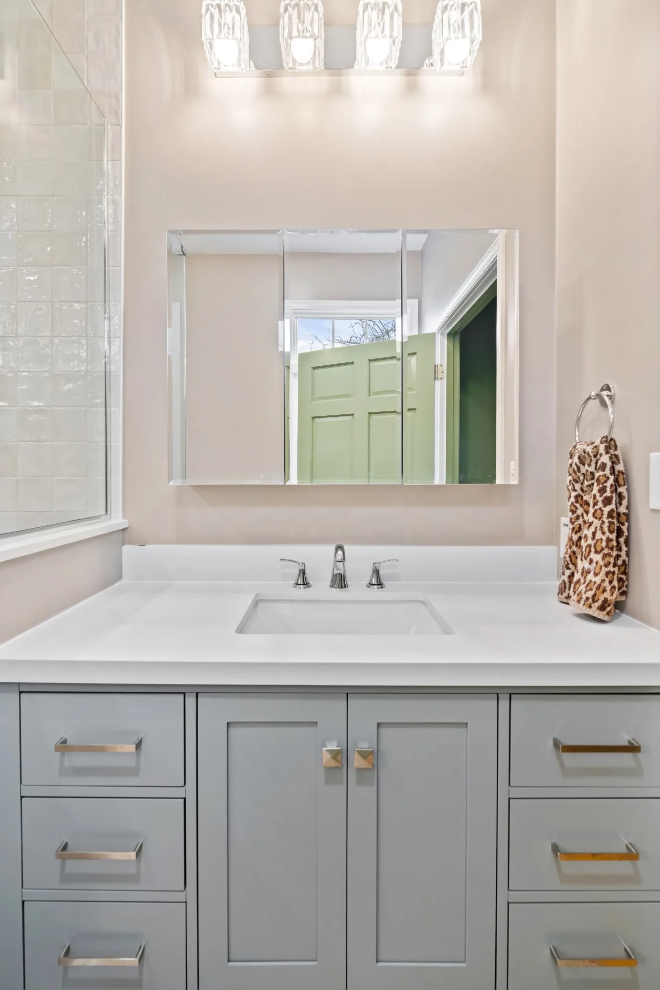 Gray Shaker vanity with a white countertop, undermount sink and three-panel mirrored medicine cabinet