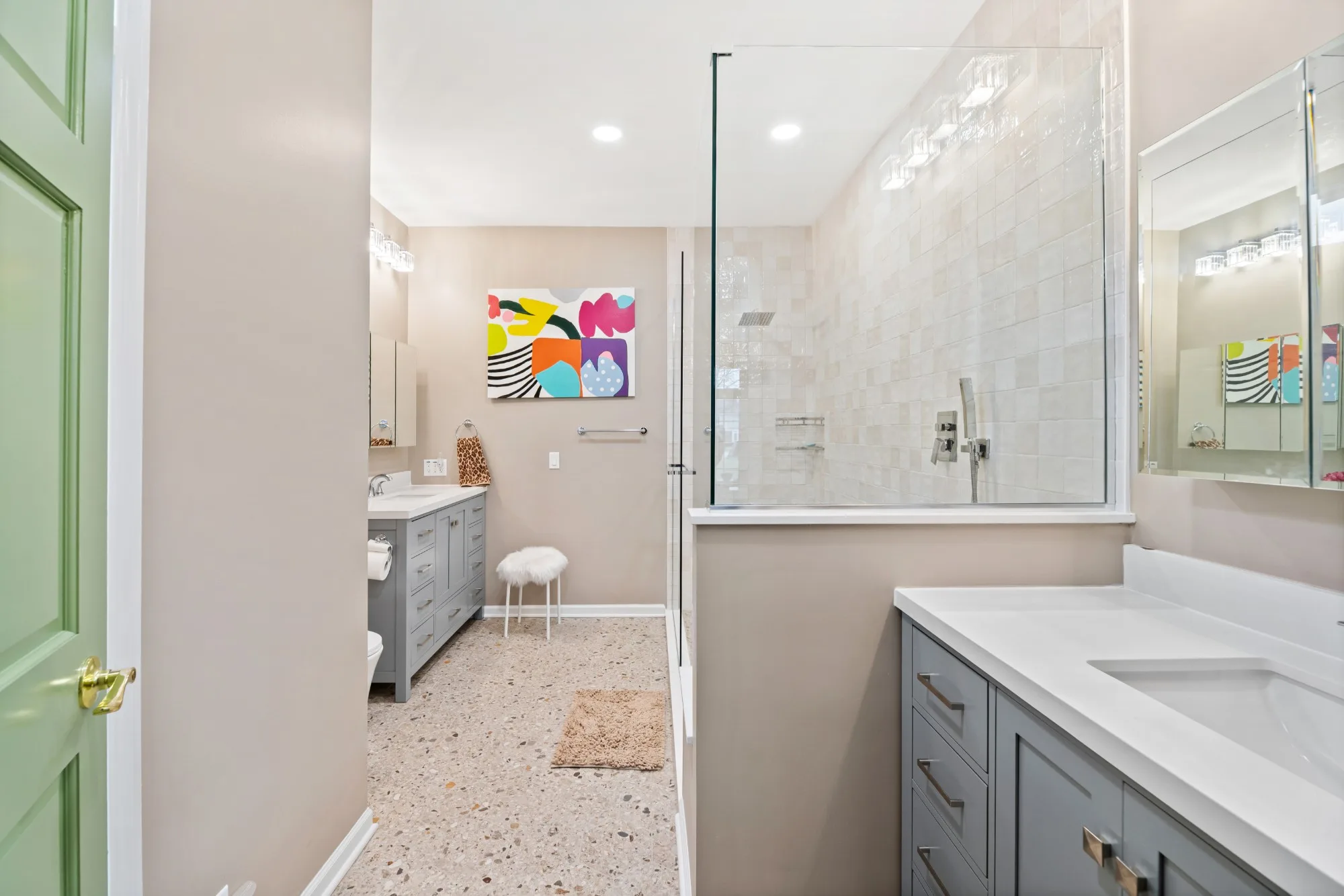 Northbrook primary bathroom with two gray Shaker vanities, a glass walk-in shower with cream tile and a terrazzo-style floor