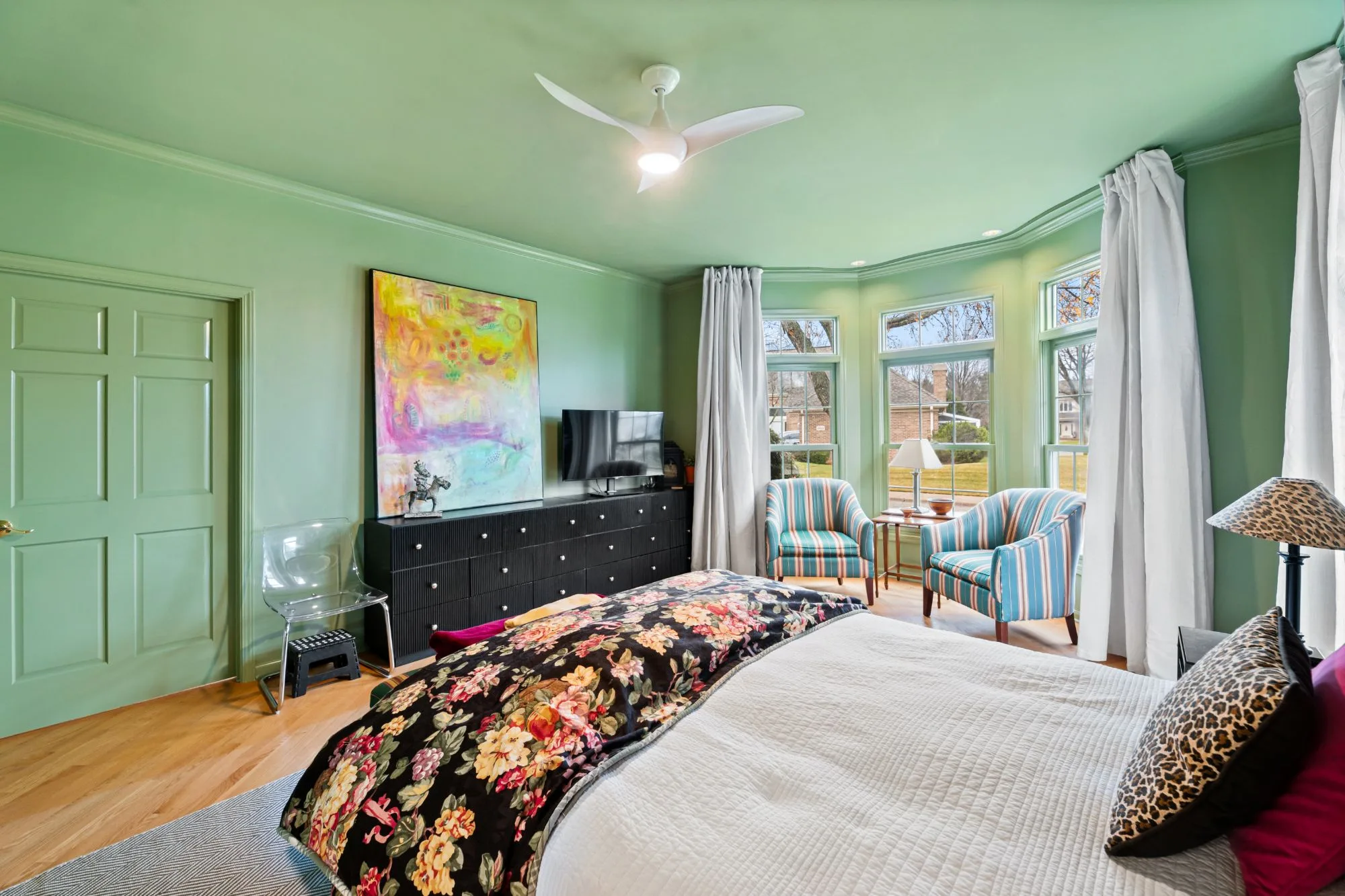Sage-green primary bedroom with painted crown molding, six-panel door and oak flooring