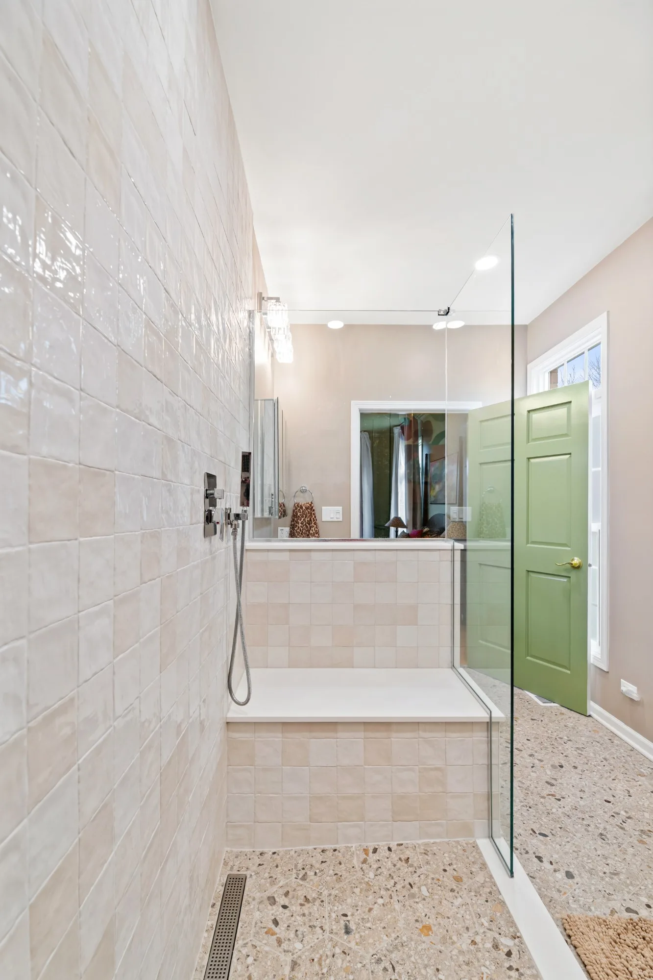 View from inside the tiled shower toward the bench and the sage-green bedroom door
