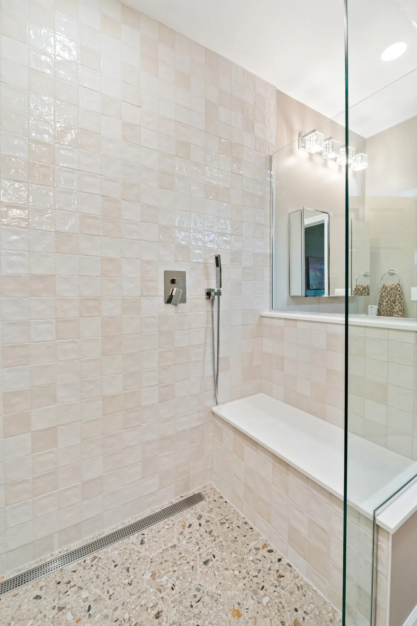 Tiled shower bench with a white top, a handheld shower and a stainless linear drain