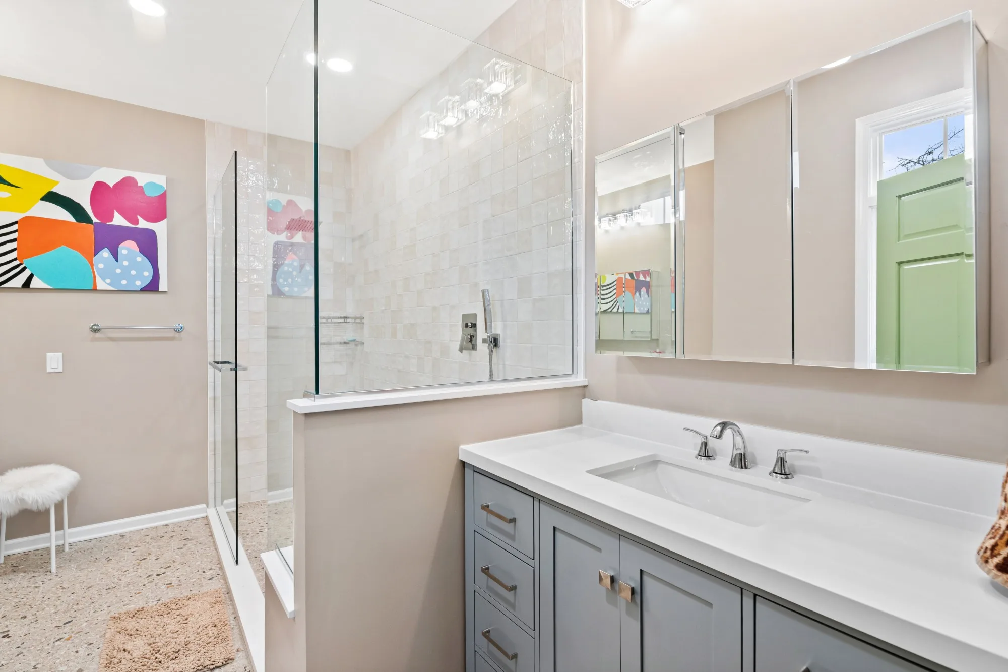 Gray vanity beside a glass-topped knee wall that encloses the walk-in shower