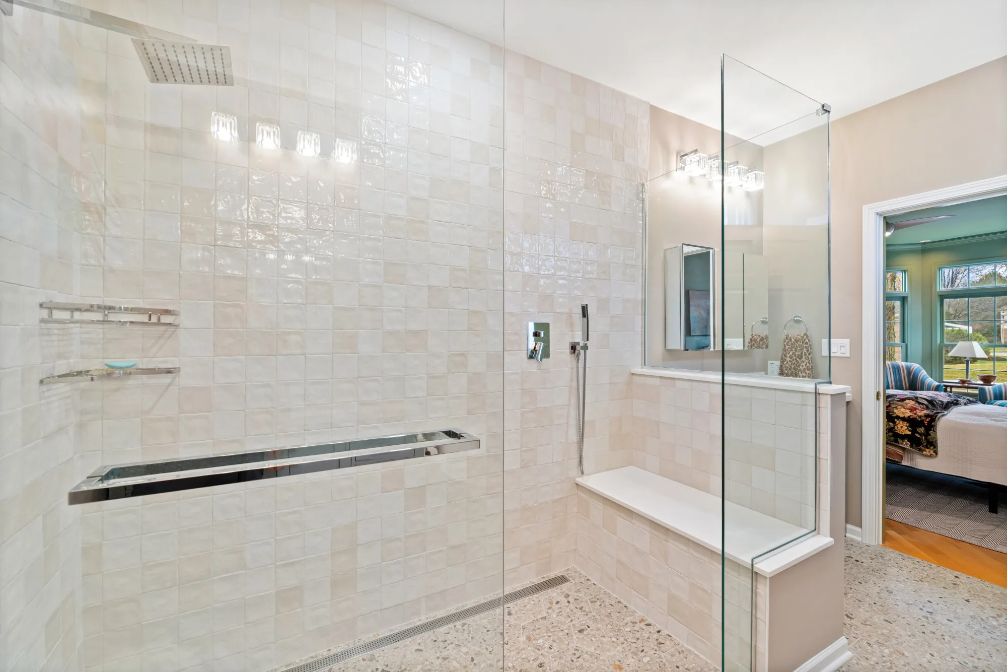 Walk-in shower with a towel bar and bench, with the primary bedroom visible through the doorway