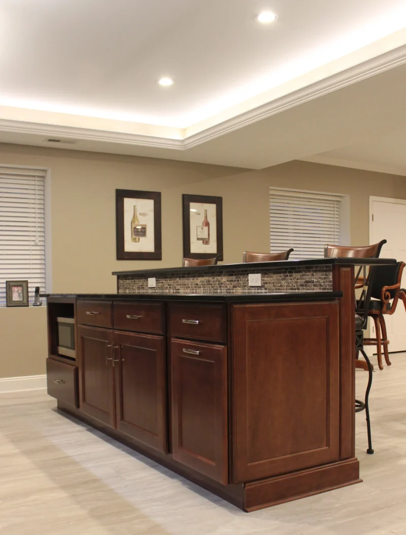 Finished basement with a cherry wet bar island, raised counter with stone mosaic backsplash and a tray ceiling with cove lighting