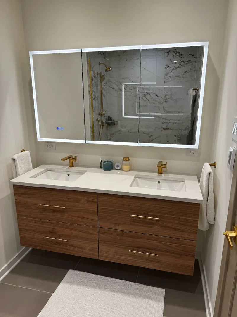 Bathroom with a walnut floating double vanity, white quartz top, brushed brass faucets and a lighted mirror cabinet