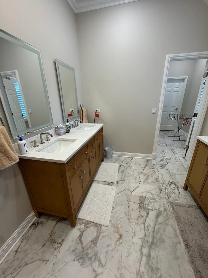 Bathroom with a wood double vanity, quartz top, lighted mirrors and large marble-look floor tile