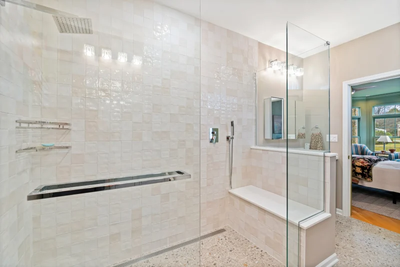 Ensuite walk-in shower with handmade ivory tile, a built-in bench and linear drain, looking through the doorway into the green bedroom