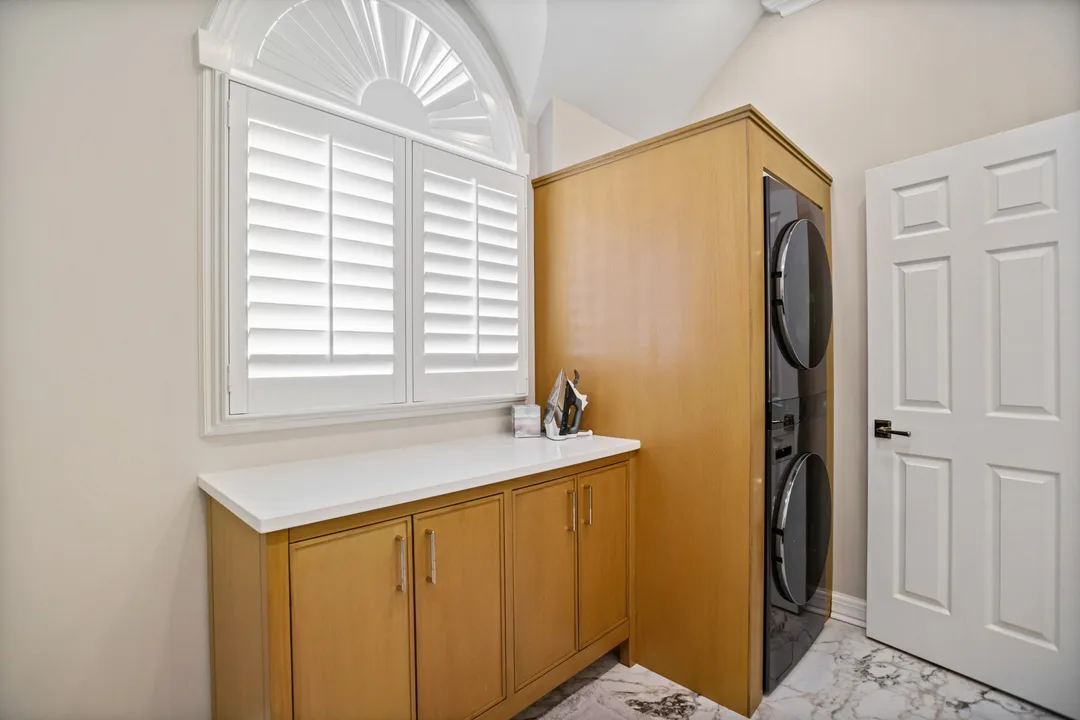 Laundry room with a stacked washer and dryer in a wood cabinet surround, base cabinets with a white quartz counter, and plantation shutters