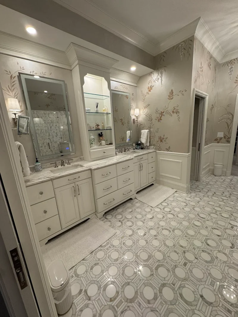 Primary bathroom with hand-painted botanical walls, white double vanity with glass-shelf tower, wainscoting and marble mosaic floor