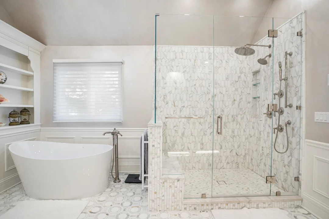 Primary bathroom with freestanding tub, frameless glass shower in marble mosaic tile with a bench, and paneled wainscoting