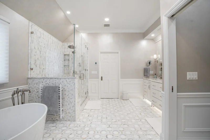 Marble primary bathroom with a freestanding tub, frameless glass shower, white vanity and marble mosaic floor