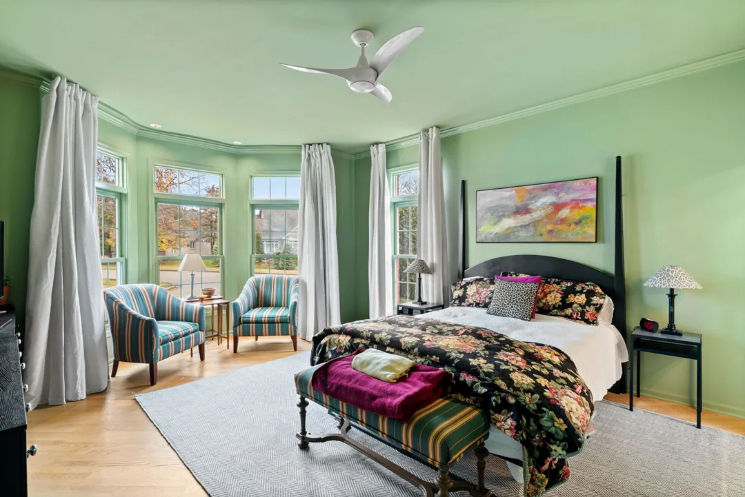 Primary bedroom painted green with crown molding, bay window seating area and ceiling fan