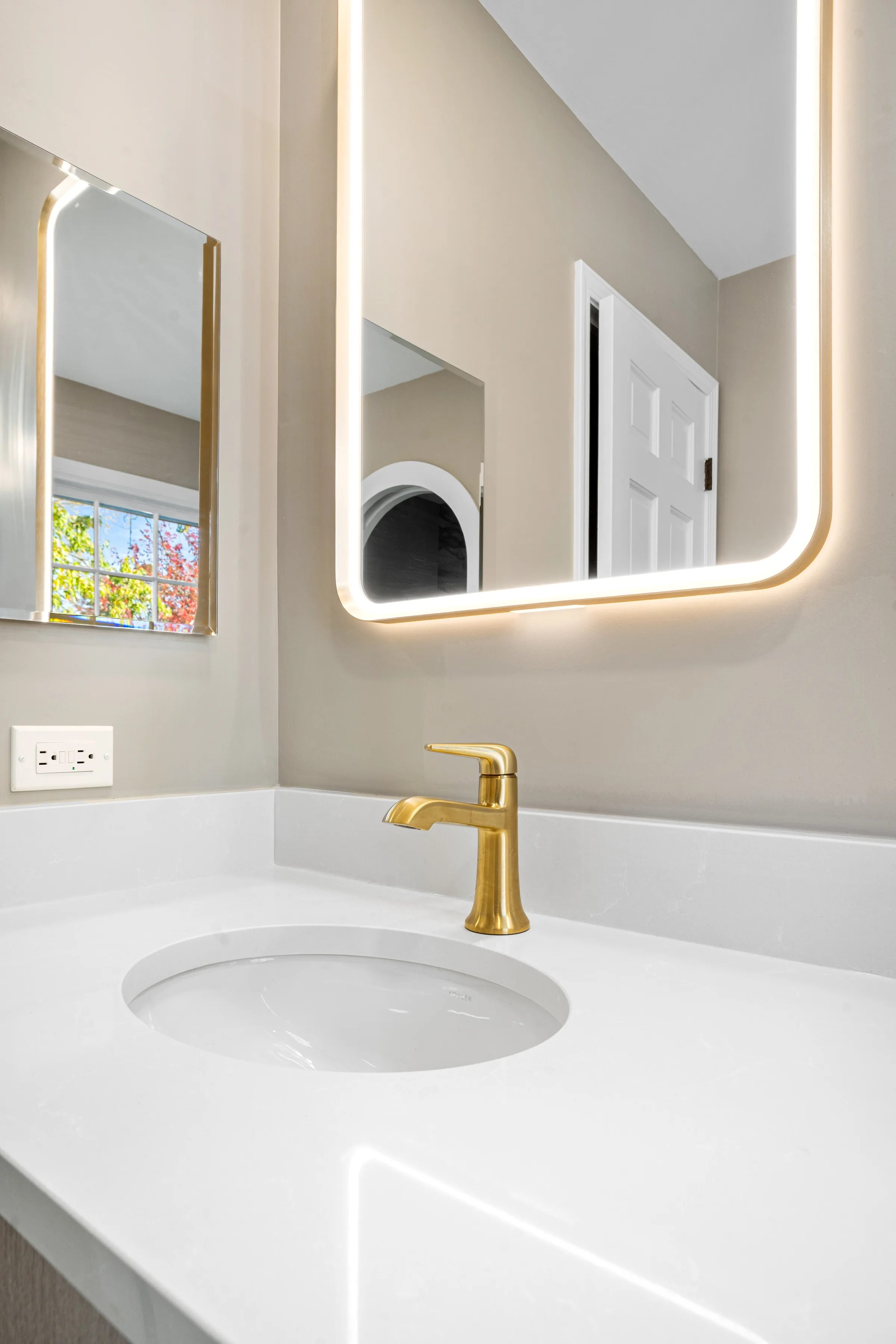 Lake Forest bathroom remodel: backlit arch mirror detail with brass sconce